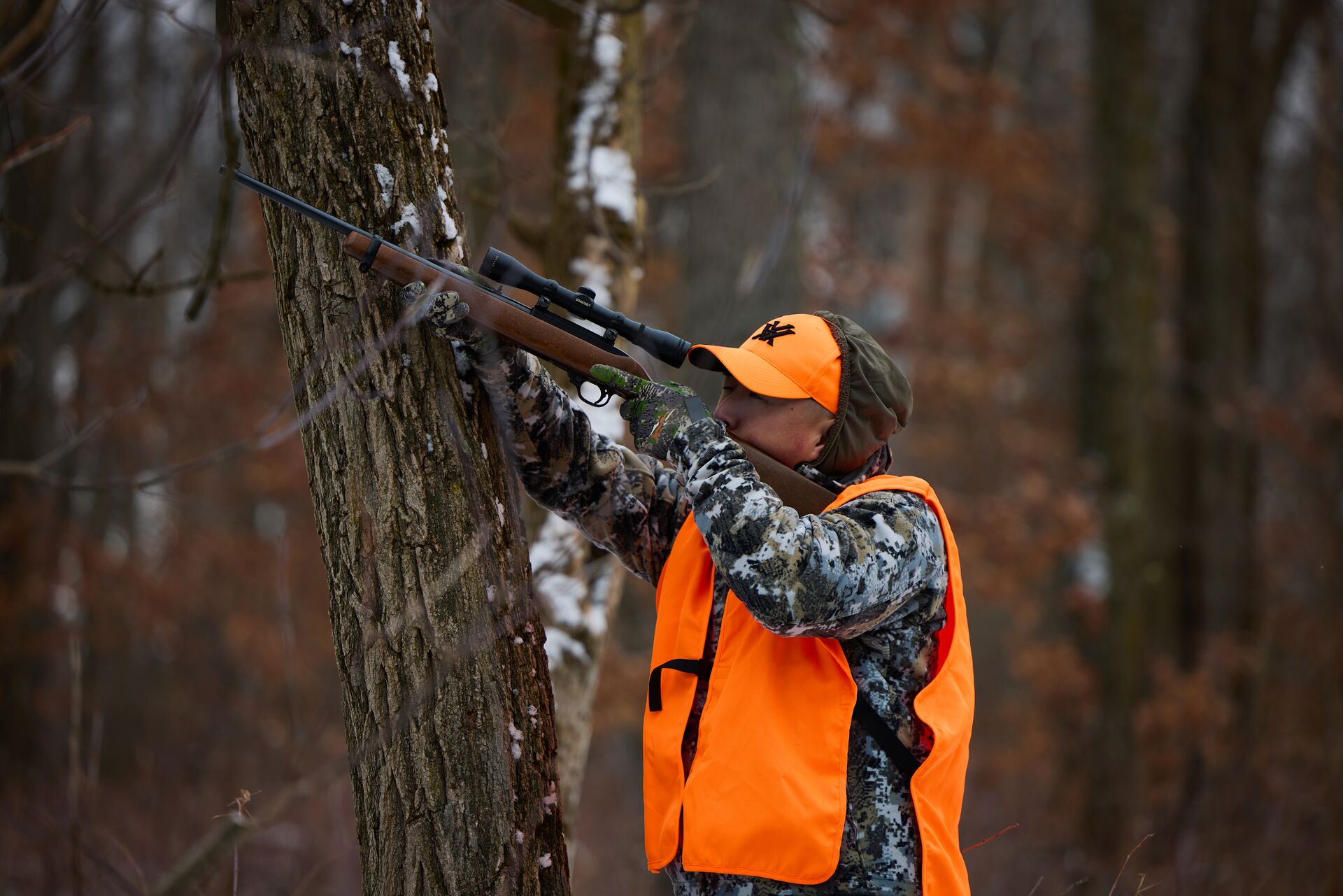 Hunter in blaze orange aiming from an autumn tree stand