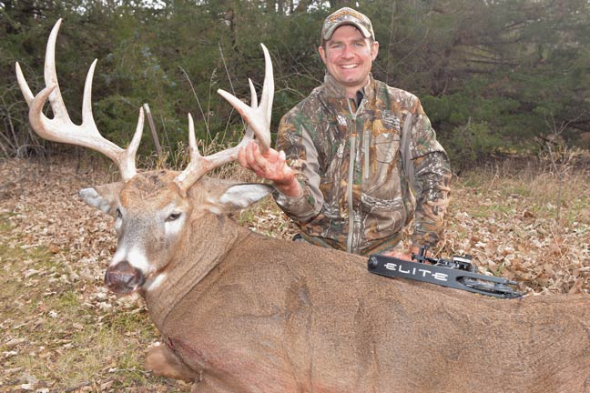 Hunter kneeling beside a harvested whitetail buck with a crossbow